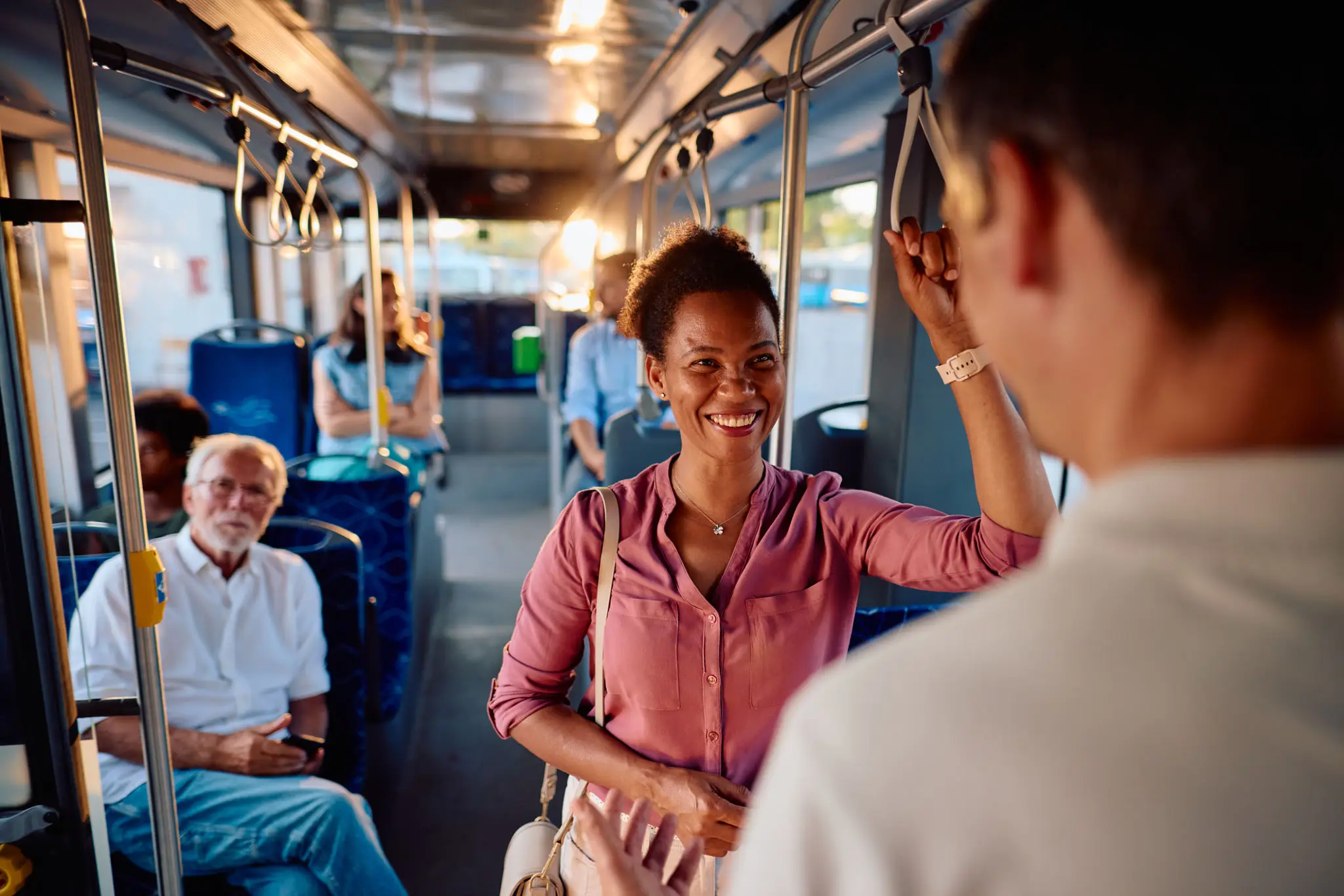 A young woman smiling and greeting a man on a bus.